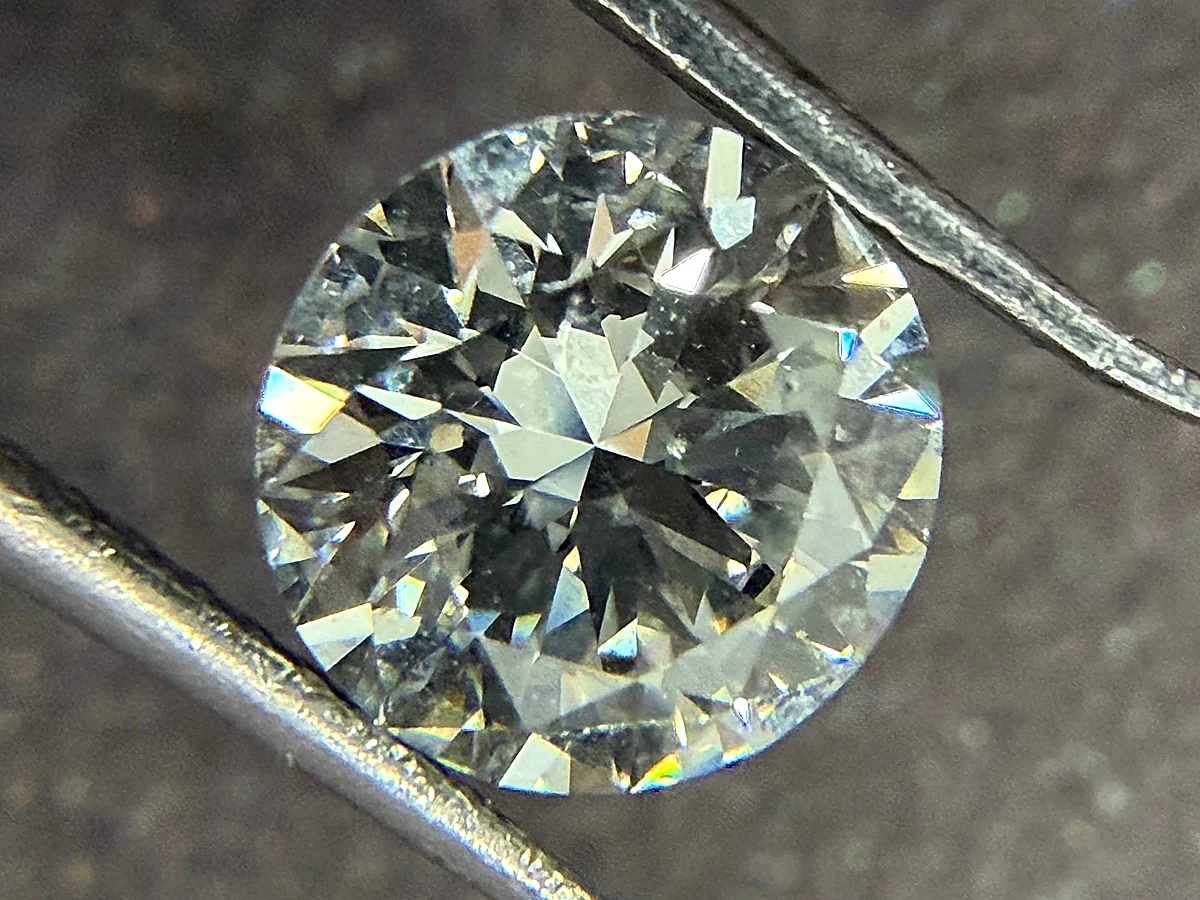 Loose round brilliant cut diamond held in diamond tweezers, showing facet pattern and light return under magnification